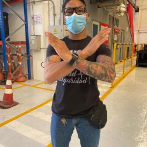 Man wearing a surgical mask and glasses in an industrial setting, crossing his arms