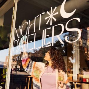 A person cleaning a window of a store called Night Dwellers.