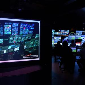 In a dark room people watching multiple monitors.