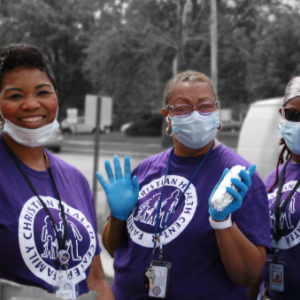 three people in protective masks and gloves outside. Each wearing a Family Christian Health Center tshirt.