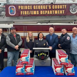 A line of people standing in front of a fire truck with a banner "Prince George's county fire/ems department". A table with smoke detectors in front of them.