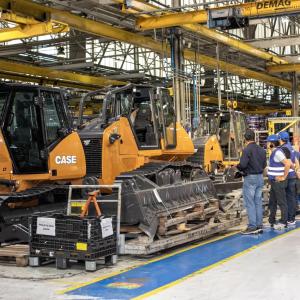 People stood wearing safety hats looking at tractors inside a factory