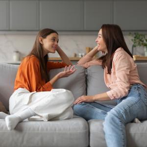 A mom and her daughter having a chat while sitting on a couch.