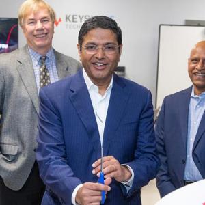Five people in a door way, the middle person holding scissors having just cut a ribbon with Keysight logos on it.
