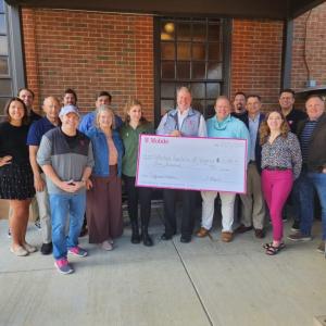 A group of people posed with a large check. A brick building behind them.