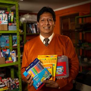 Fernando holding art supplies. Shelves of art and office supplies behind him.