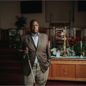 Photo of Jonathan; he is holding a walking stick as an aid to his blindness.