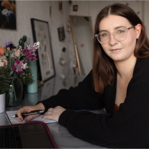 Photo of Simone shown seated at her desk writing.