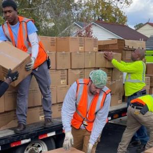 Volunteers wearing safety vests unloading boxes off a trailer.