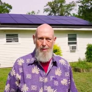 Marc Thomas stands in front of his house which has solar panels on the roof.