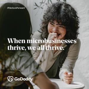 GoDaddy: Venture Forward. When microbusinesses thrive, we all thrive. Photo of two women seated at a small table.
