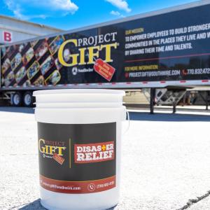 a white bucket with "GIFT disaster relief" label. A trailer in the background with "Project GIFT" on the side