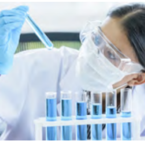 A person in protective lab gear looking at a small tube of blue liquid.