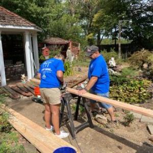 two people cut wood on saw horses