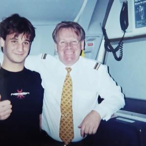Two people stood next to each other smiling inside an aeroplane 