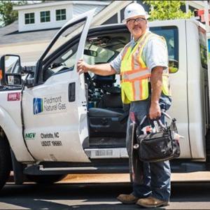 A utility worker standing with a hand on an open door to a utility truck in a residential area.