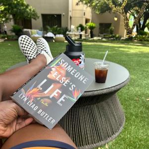 Geoffrey Brown reading a book in his back yard with his feet on a table.