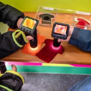 Two students use microscopes to examine the fibers of two t-shirts through an interactive experiment.