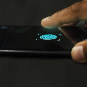 A close-up of a finger poised to tap a fingerprint scanner icon on a smartphone screen, indicating biometric authentication.