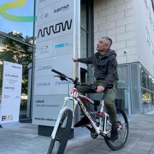 Giuliano Rapetti on a bicycle, pointing to a sign for Arrow.