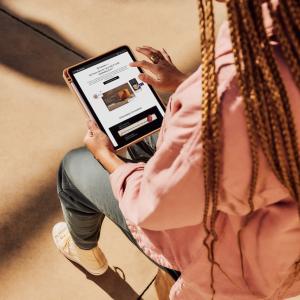 Woman seated on a chair and reading a tablet.
