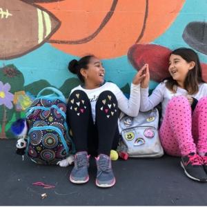 Photo of two young girls seated and giving a high five.