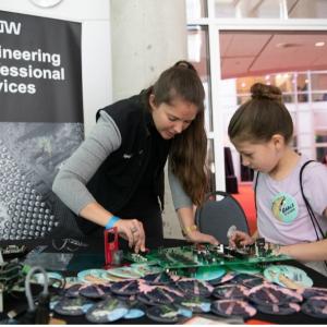Grace Doepker at an Engineering professional services stand showing a young child some equipment