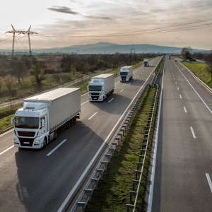A row of semi trucks on a highway. Powerlines to the side and a scenic background.