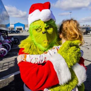 A person dressed as the Grinch hugging a child outside