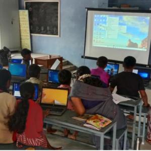 classroom of students sat at tables working on laptops 