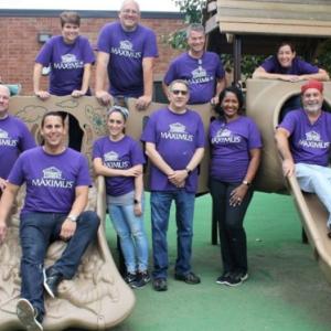 A group of people stood around a children's climbing frame, wearing purple MAXIMUS t-shirts