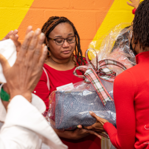 A young woman is receiving a gift from Santa Claus. Santa Claus is giving another girl a high-five. A woman is accepting a package from another woman.