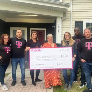A group of people posed with a large check. A home behind them.
