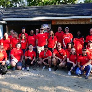 Group of people in red shirts posing in front of home being built