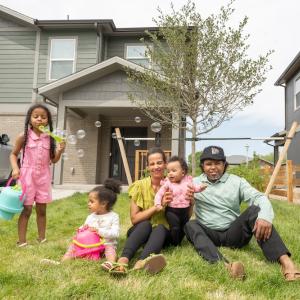 Family of parents and three children sitting in front of house blowing bubbles
