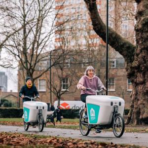 Two people riding cargo bikes through a park.