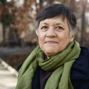 Person stood outside in front of trees, wearing a green scarf 