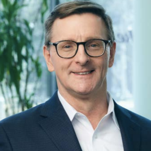 Headshot of a person wearing glasses, stood in front of a plant