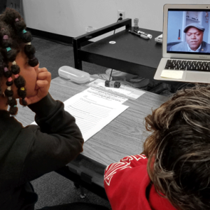 two students at a desk watch a video on a laptop