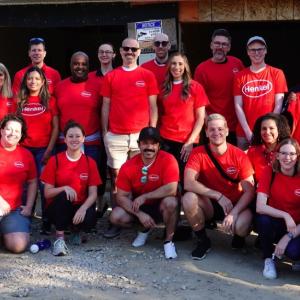 group of people outside a home being built, all are wearing matching orange shirts with Henkel logo