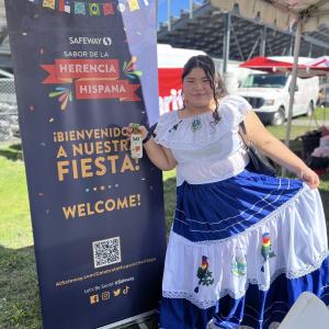 Photo of person dressed in traditional Hispanic clothing in front of Safeway welcome sign displayed in Spanish and English languages