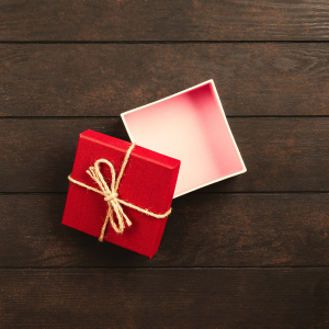 A small, red, square gift box sits opened on a dark wooden table.