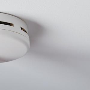 Fire Safety Month: Finger shown pushing the button on a smoke detector.