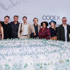 Group of 11 women and men stand behind a model of 3D-printed homes