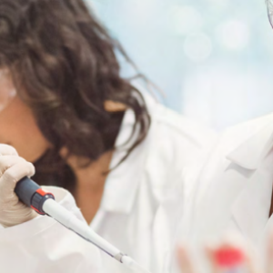 Three people in protective lab gear. One holds a pipette.
