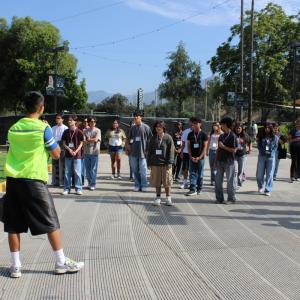 Students gather outdoors while a staff member leads a walking tour of the festival grounds, with trees and venue infrastructure visible in the background.