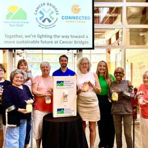 Members from Cancer Bridges, Connected Energy Solar, and Green Mountain Energy Sun Club smiling with solar mason jars and a life-size light switch.
