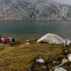 People at the edge of a body of water in mountainous terrain.