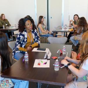 Participants sit around a table during a collaborative workshop, with notebooks, markers, and water bottles spread across the table in a modern meeting room.