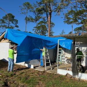 Volunteers putting a tarp over a storm damaged home